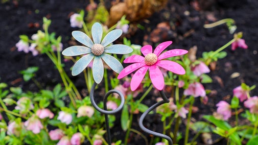 Two steel daisies stand next to each other against greenery